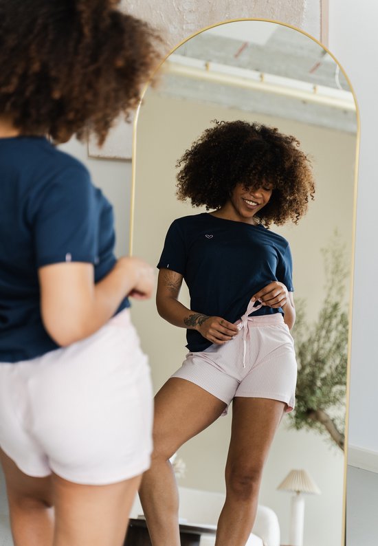 Model kijkt in de spiegel, draagt een donkerblauwe pyjamatop met een klein hartje en een roze gestreepte pyjamashort met strik.