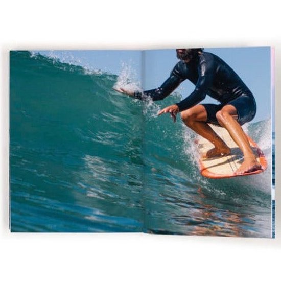 Een surfer in een zwart wetsuit surft op een golf op een oranje en wit surfboard.