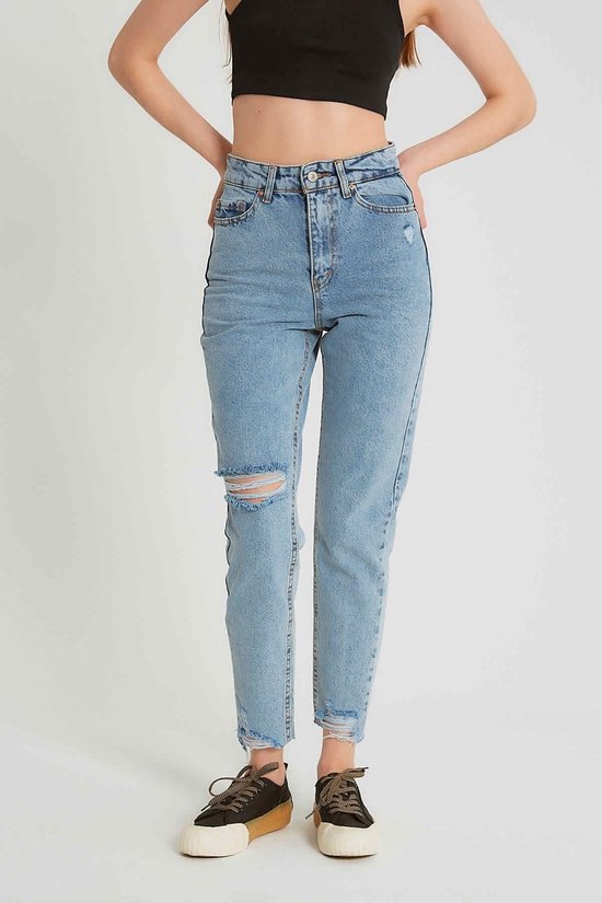 Model draagt een lichtblauwe spijkerbroek met hoge taille, gescheurde knie en rafelige zoom. Ze draagt een zwarte crop top.