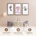 Drie ingelijste prints: een babyvoetje, een baby met roze muts en een handafdruk. Daaronder decoratie.