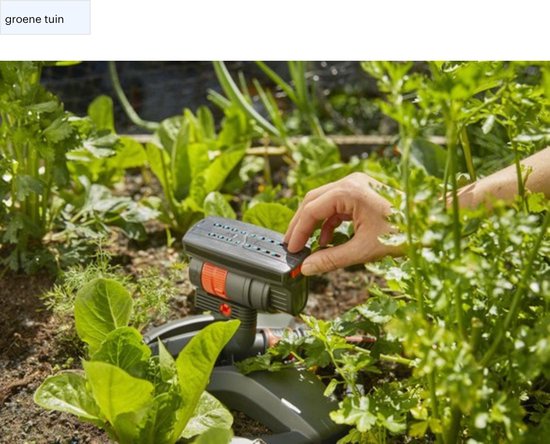 Une main ajuste l'arroseur oscillant GARDENA dans un jardin verdoyant.