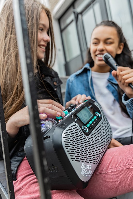 Twee lachende tienermeisjes, één met zwarte leren jas, de ander met spijkerjasje, bij VTech Super Sound Karaoke.