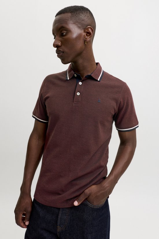 Man met bordeauxrode polo, witte en marine kraag- en mouwboorden. Een hand in de zak.
