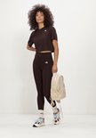 Model met bruine Adidas legging, crop top en beige rugzak.