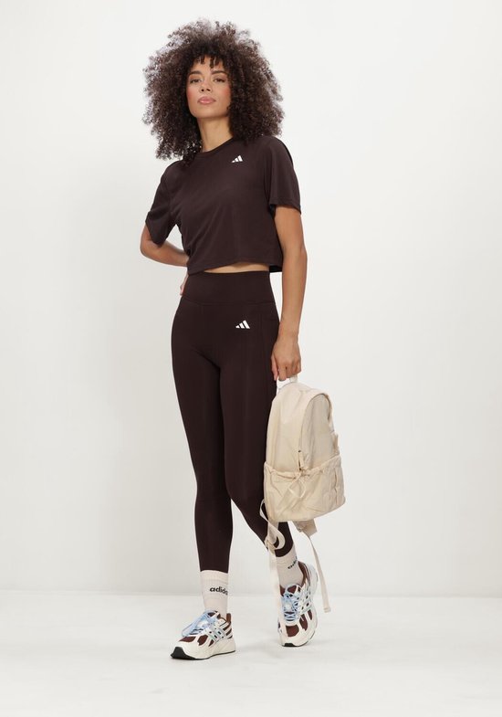 Model met bruine Adidas legging, crop top en beige rugzak.