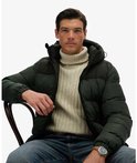 Man met beige coltrui en donkergroene jas met capuchon, zittend.
