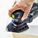 Een hand bedient een zwarte schuurmachine met groen accent bij het schuren van een witte hoek.