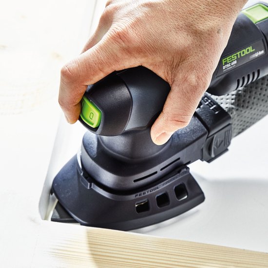Een hand bedient een zwarte schuurmachine met groen accent bij het schuren van een witte hoek.