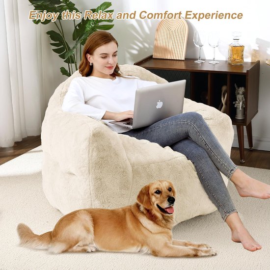 Een vrouw zit op een crèmekleurige, pluizige zitzak met een laptop. Een golden retriever ligt voor de zitzak.
