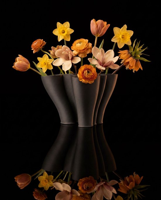 Zes zwarte, 3D-geprinte vazen met golvende vormen, gevuld met oranje en gele bloemen.