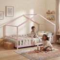 Kinderhuisbedframe in roze met spijlen, wit met houten lattenbodem en decoratie van lichtjes. Twee kinderen spelen op de grond.
