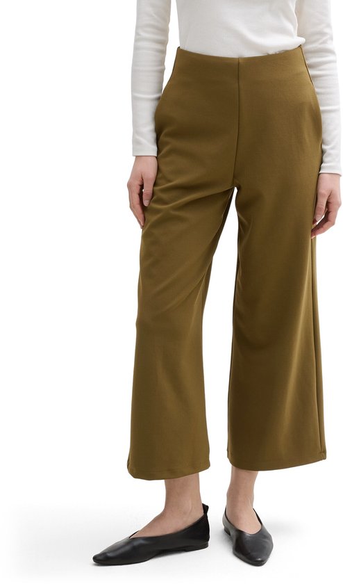 Model draagt een olijfgroene culotte met wijde pijpen en een hoge taille. Ze draagt een witte top met lange mouwen.