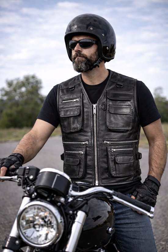 Man met baard, zonnebril en helm draagt een zwart leren vest met meerdere zakken op een motor.