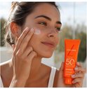 Vrouw met zonnebrandcrème op haar gezicht, houdt Lancaster Sun Beauty Face Cream SPF 50 vast.