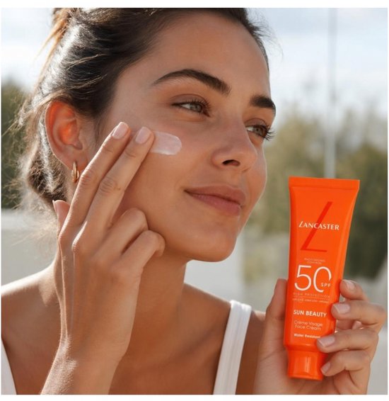 Vrouw met zonnebrandcrème op haar gezicht, houdt Lancaster Sun Beauty Face Cream SPF 50 vast.