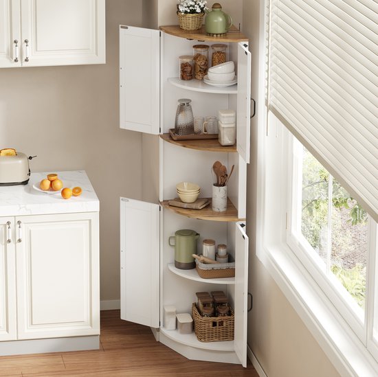 Witte hoekkast met open deuren, gevuld met keukengerei en decoraties, naast een raam met blinds en uitzicht op groen.