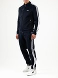 Donkerblauwe trainingsbroek met witte strepen op de zijkant, gedragen door een man met witte schoenen.