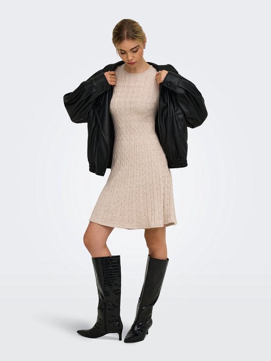 Model met beige gebreide jurk met kabelpatroon en zwarte leren jas.