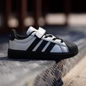 Zilveren Adidas kindersneaker met zwarte strepen, klittenband en zwarte neus.