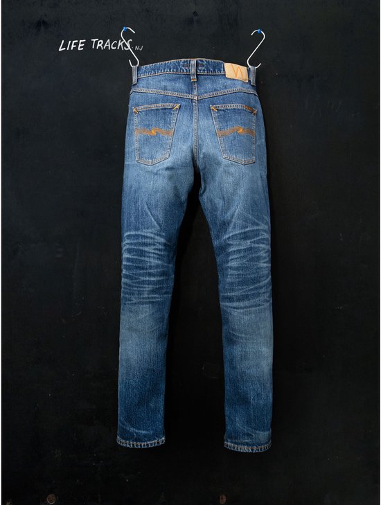 Achterkant van Nudie Jeans met "LIFE TRACKS" tekst, bruin leren label en kenmerkend oranje stiksel op de zakken.