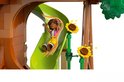 Meisje met bruin haar glijdt van groene glijbaan, met gele en oranje linten, omringd door LEGO-elementen zoals zonnebloemen.