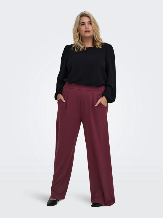 Vrouw met zwarte blouse en bordeauxrode wijde broek met plooien en steekzakken.