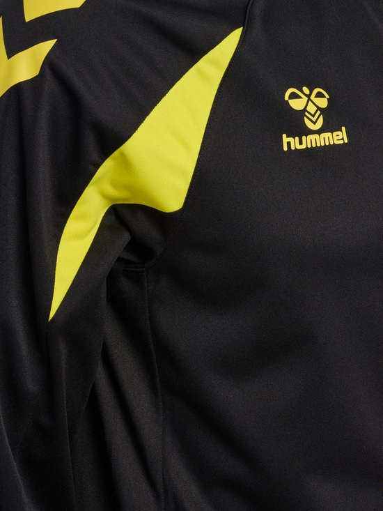 Close-up van de schouder en borst van een zwarte Hummel trainingsjas met gele accenten en logo.