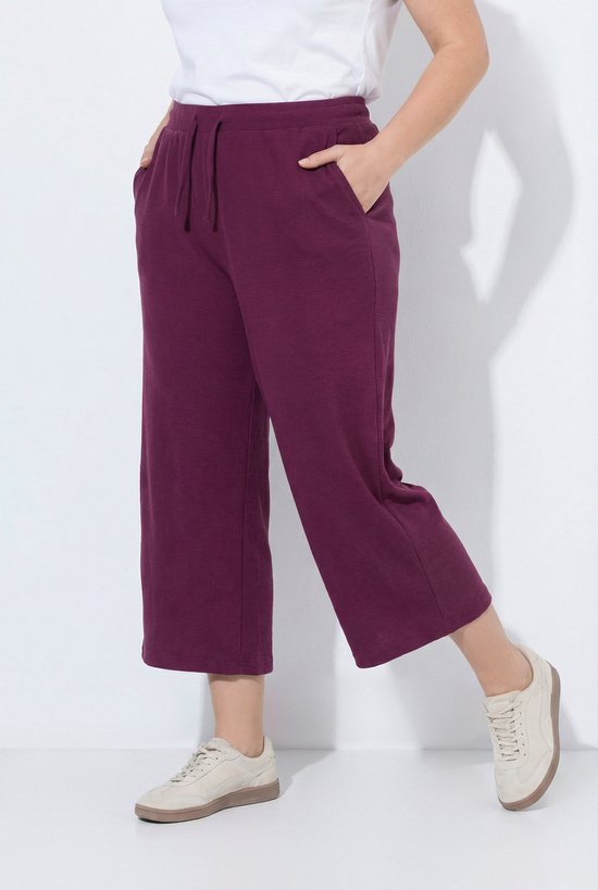 Model draagt een donkerrode sweatculotte met wafelstructuur, wijde pijpen en zakken.