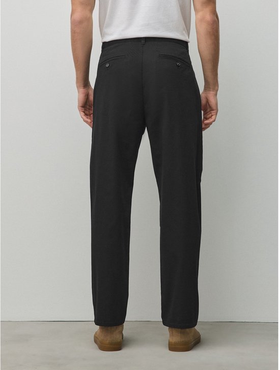 Achterkant van een zwarte chino broek met twee paspelzakken met knoop op een model.