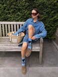 Een vrouw zittend op een bankje buiten, met spijkerjurk, lichtblauwe sokken met ruitenpatroon en bruine instappers.