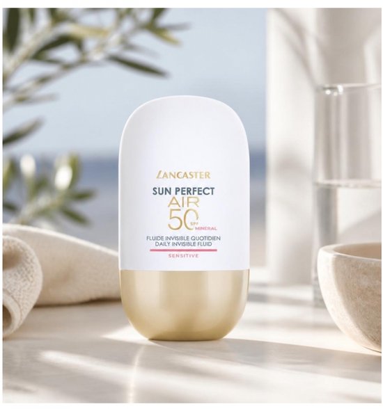 Lancaster Sun Perfect AIR SPF 50 Mineral sensitive, witte dop met gouden basis, naast een handdoek en een stenen kom bij zee.