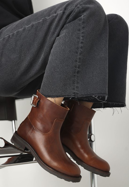 Cognac leren enkellaars met gesp, gedragen door een zittend model met cropped jeans.