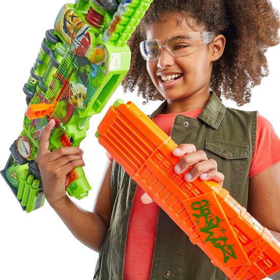 Meisje met beschermende bril houdt een felgroene Nerf Zombie Corrupter blaster en een oranje magazijn, lachend naar de camera.