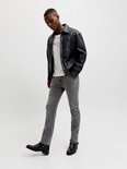 Man met zwarte leren jas, wit T-shirt en grijze jeans.