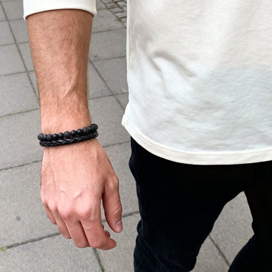 Zwarte lavasteen armband met gevlochten leer, gedragen om een pols.