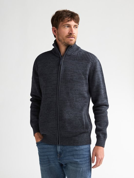 Man met blauwe jeans draagt donkerblauw gemêleerd gebreid vest met ritssluiting, hoge kraag en steekzakken.