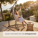 Vrouw in witte badjas ontspant in crème hangmat op een houten terras met uitzicht op zee.