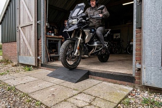 Zwarte rubberen drempelhulp van 60 cm breed en 10 cm hoog met antislipprofiel, een motorrijder rijdt de schuur op.