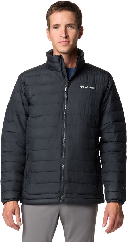 Homme portant une veste Columbia Powder Lite de couleur foncée avec fermeture éclair, col montant et matelassage horizontal. T-shirt gris et beige et pantalon gris.