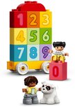 Toren van gestapelde gekleurde blokken met cijfers 0 t/m 9 op een gele wagon. Twee kinderen en een hondje.