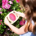 Enfant tenant un kaléidoscope en bois devant un rosier rose.