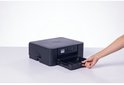 Een hand trekt de papierlade uit een zwarte Brother multifunctionele printer.