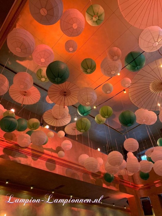 Veel ronde papieren lampionnen in groen en wit en papieren parasols hangen aan het plafond. Oranje verlichting.