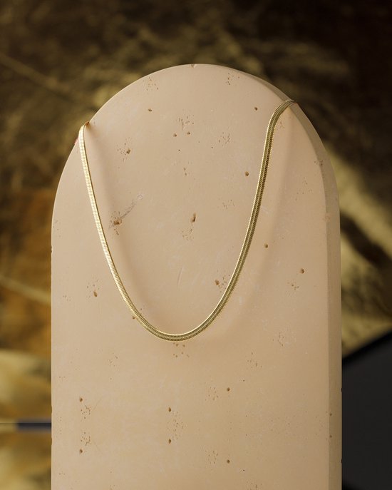 Gouden slangenketting gedrapeerd over een beige, organisch gevormde display.