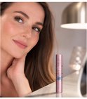 Vrouw met lange wimpers kijkt omhoog, naast een roze mascara koker met 'SKY HIGH'.