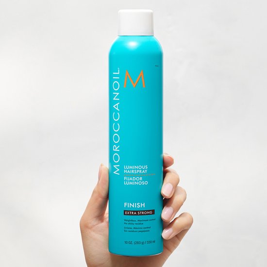 Turquoise Moroccanoil haarlakfles met witte dop, vastgehouden door een hand.
