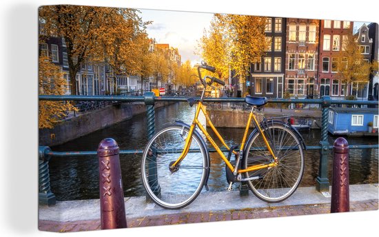 Canvas Schilderij Fiets voor de gracht met uitzicht op Amsterdamse architectuur - Wanddecoratie