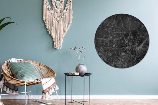 Décoration murale ronde noire aspect cuir avec subtils détails griffés, au-dessus d'un fauteuil en rotin avec coussins.
