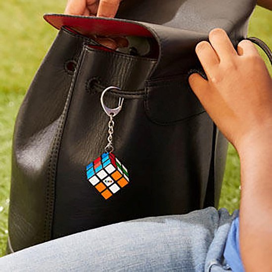 Rubik's Cube sleutelhanger aan een zwarte tas, gedragen door iemand in een spijkerbroek.