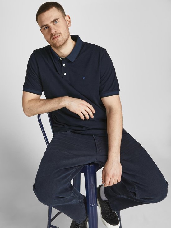 Zittend model in donkerblauwe polo met contrasterende kraag en manchetten. Logo op de borst.